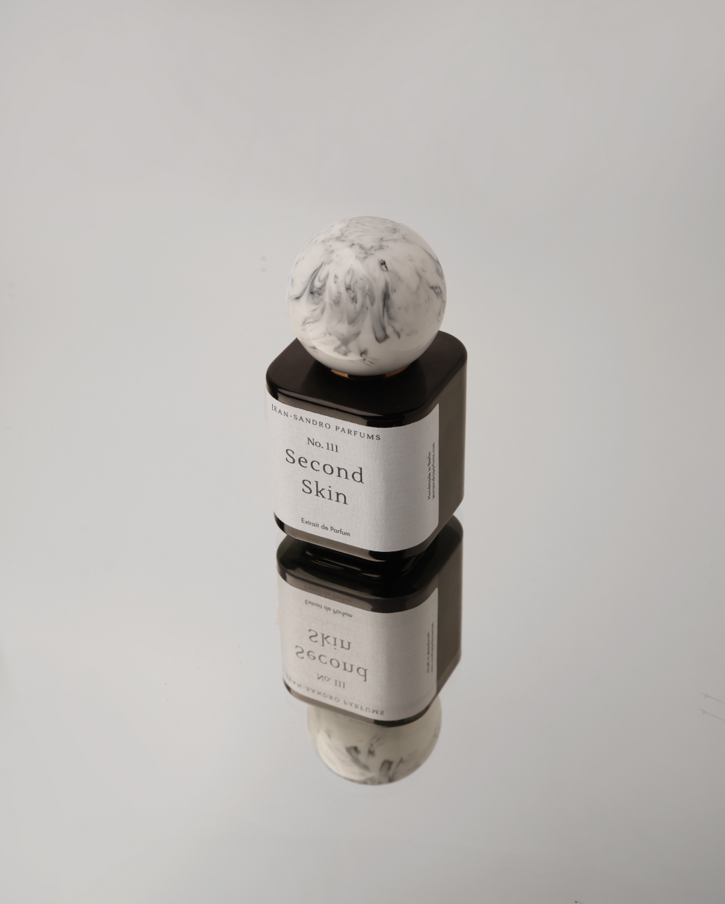 A cosmetic product container with a white marble-patterned sphere cap, stacked on top of a black rectangular base. The label reads 'The Ordinary Cosmetics No.