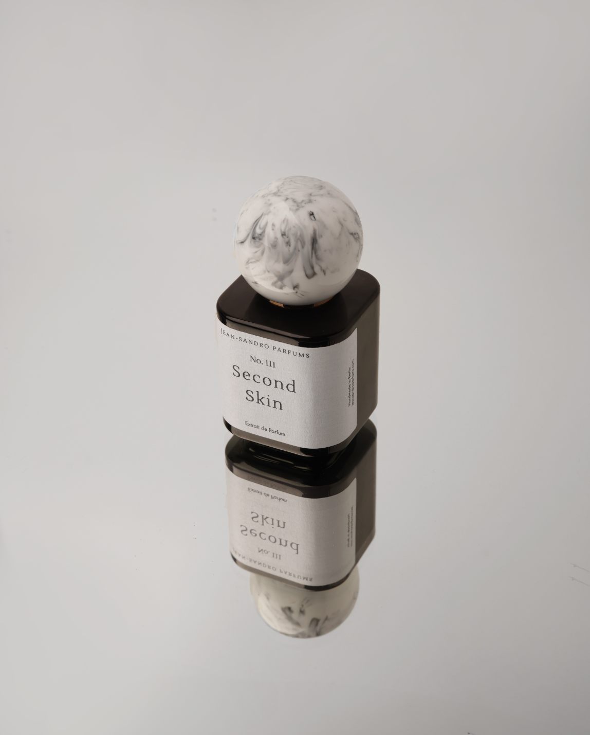 A cosmetic product container with a white marble-patterned sphere cap, stacked on top of a black rectangular base. The label reads 'The Ordinary Cosmetics No.