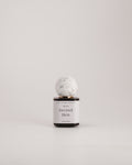 A small cylindrical bottle with a white label reading 'Second Skin' and 'Gentle Handmade Perfumes' near the top, topped with a round white marble-like cap, centered on a light gray background.