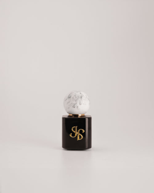 A luxury cosmetic bottle with a glossy black base, a white marble top, and gold monogram lettering on the front, set against a clean light gray background.