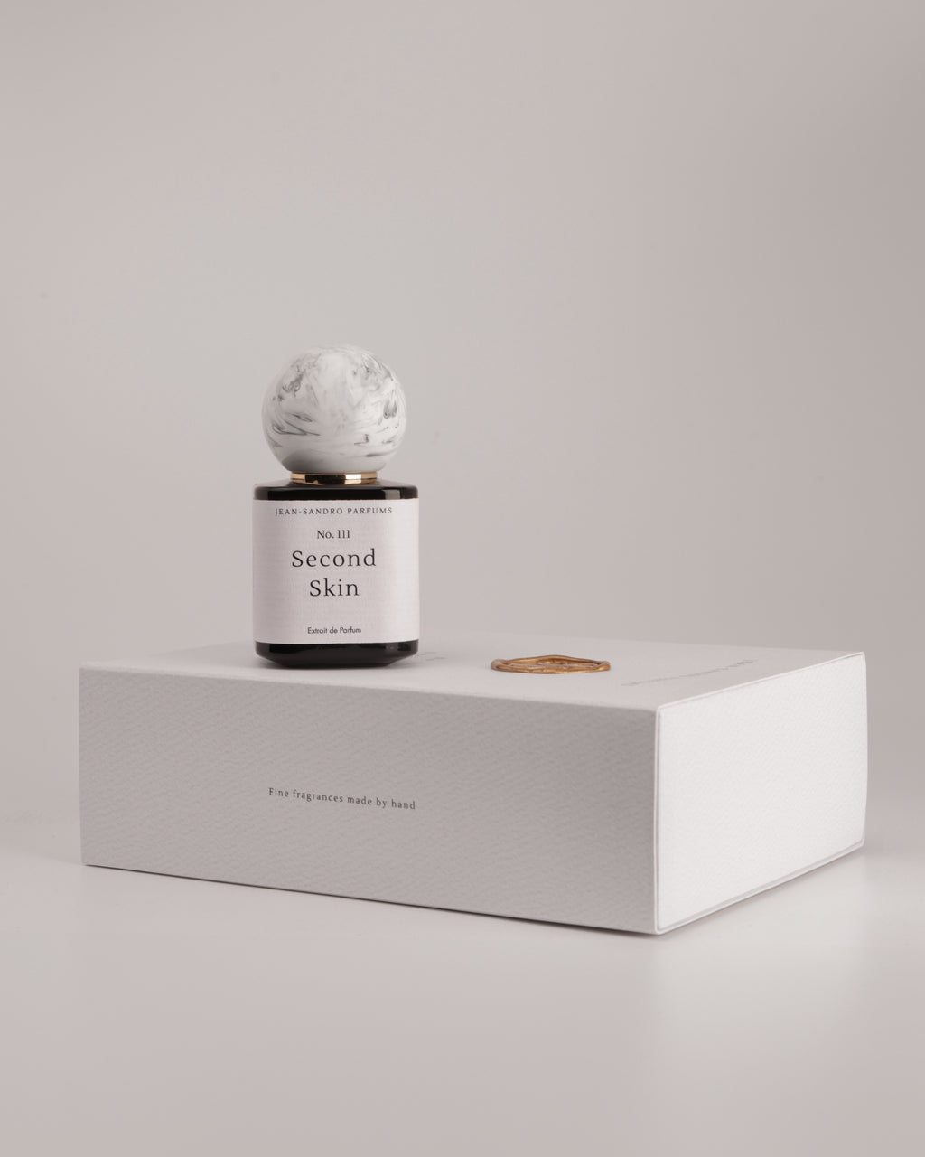 A reed diffuser bottle with a white marble sphere top and a black base, labeled 'Second Skin' by Second Skin Fragrance, displayed on top of a white textured box against a neutral light gray background.
