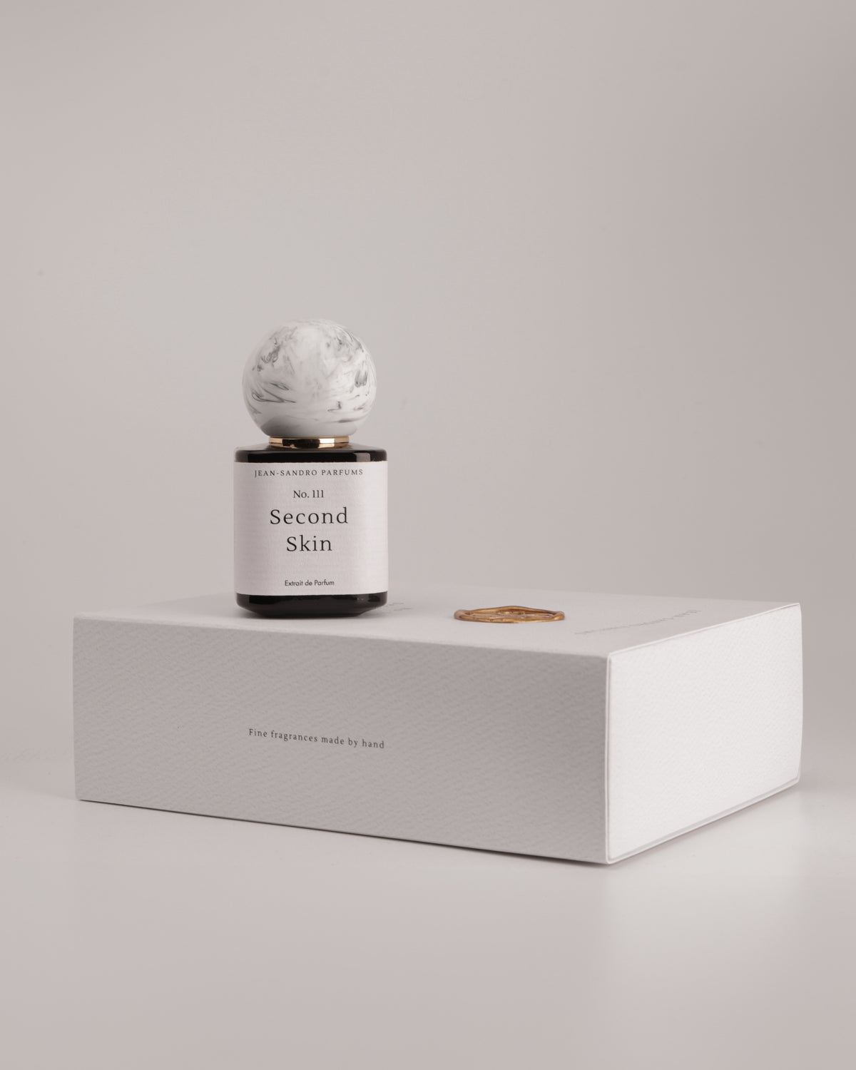 A reed diffuser bottle with a white marble sphere top and a black base, labeled 'Second Skin' by Second Skin Fragrance, displayed on top of a white textured box against a neutral light gray background.