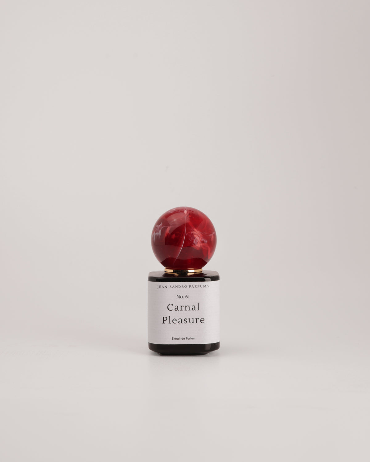 A small perfume bottle with a spherical red marbled cap and a white label reading 'Carnal Pleasure' by Sweet Fantasy Perfumes, centered on a light gray background.