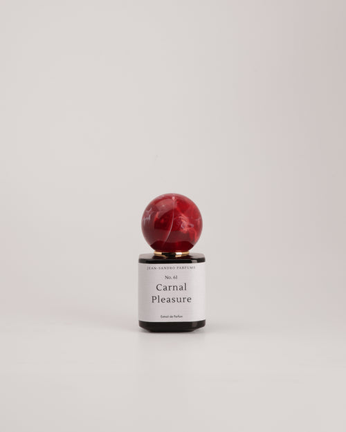 A small perfume bottle with a spherical red marbled cap and a white label reading 'Carnal Pleasure' by Sweet Fantasy Perfumes, centered on a light gray background.