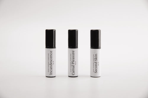 Three small cylindrical cosmetic tubes with black caps and white bodies, arranged side by side on a light gray background. The labels read 'Intocandescence', 'Carnal Pleasure', and 'Second Skin'.